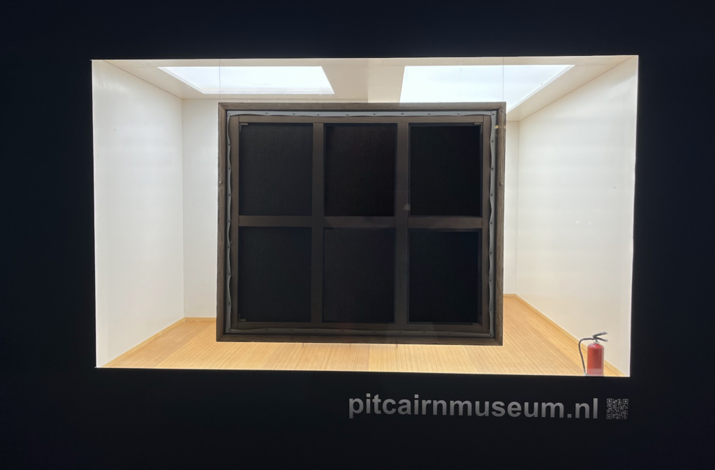 A photograph of the exhibit described in this review. We see the back of what is, relative to the scale of the space, a large canvas, and, in the corner, a tiny fire extinguisher.