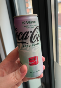 My hand, holding a can of Coke Zero K-Wave in front of the window for lighting purposes. It's an energy drink-style can, with a pastel purple to green gradient design and Korean characters on it.